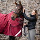 Woman petting a horse wearing a red rug in front of a stone wall.