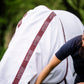 Person adjusting a white horse blanket by leader equine with red trim on a horse, set against a blurred green background.