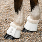 White pu leather horse boots with cream faux-fur trim with leader equine brand logo worn on a horse standing on gravel