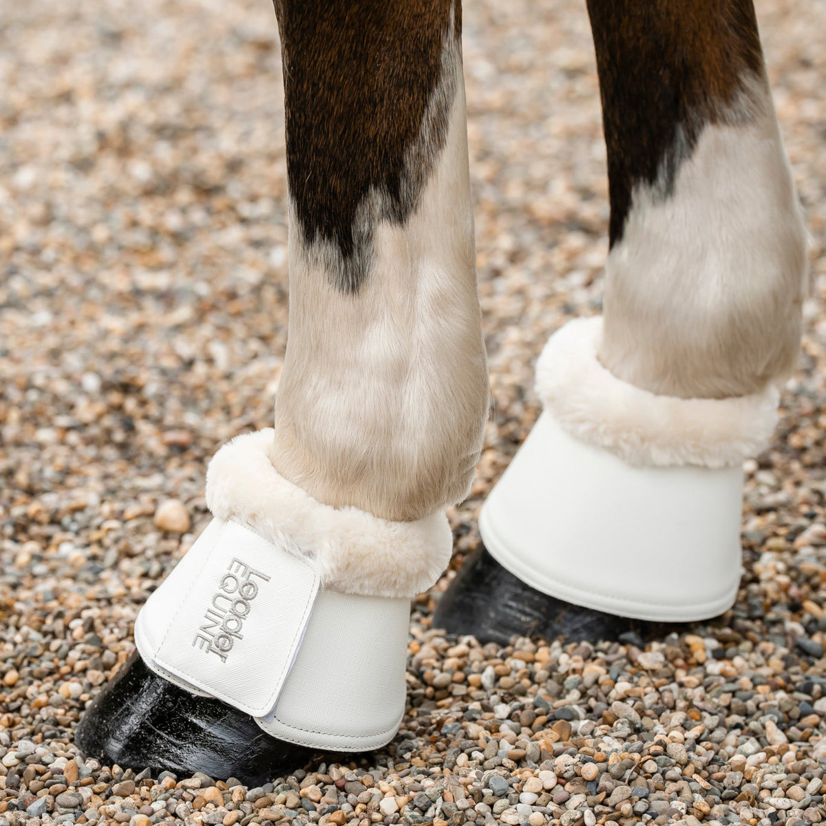 White pu leather horse boots with cream faux-fur trim with leader equine brand logo worn on a horse standing on gravel