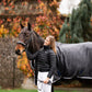 Woman wearing leader equine breeches and puffer jacket standing next to a horse wearing a Leader Equine horse rug in an outdoor setting