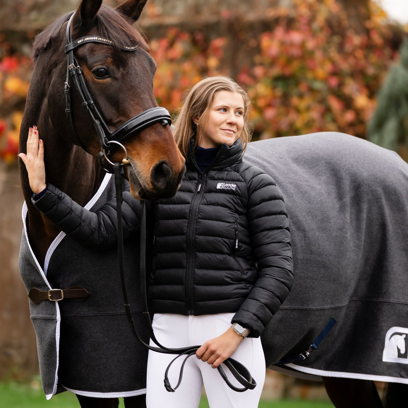 Woman standing next to a horse wearing a leader equine horse blanket with a visible brand logo.