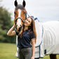 woman wearing navy polo t shirt with grey breeches standing with bay horse in white summer rug