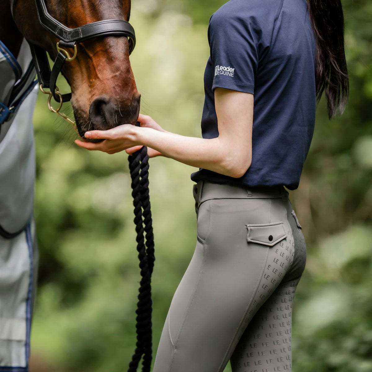 woman in equestrian breeches by leader equine and navy cotton t-shirt with horse in fly rug