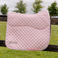 A light pink quilted equestrian saddle pad with a diamond pattern, featuring a silver embroidered Lesure logo, resting on a dark wooden fence with a blurred green field and trees in the background.