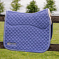 A blue quilted equestrian saddle pad with white trim and a cream sherpa lining, resting on a wooden fence with a blurred grassy field and trees in the background. The brand 'Leader Equine' is visible on the lower left corner.