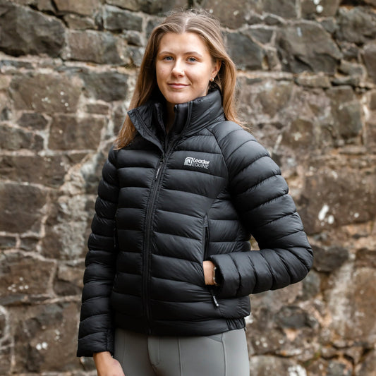 Woman wearing a black puffer jacket with a brand logo against a stone wall.