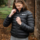 Woman wearing a black puffer jacket with a brand logo in an outdoor setting.