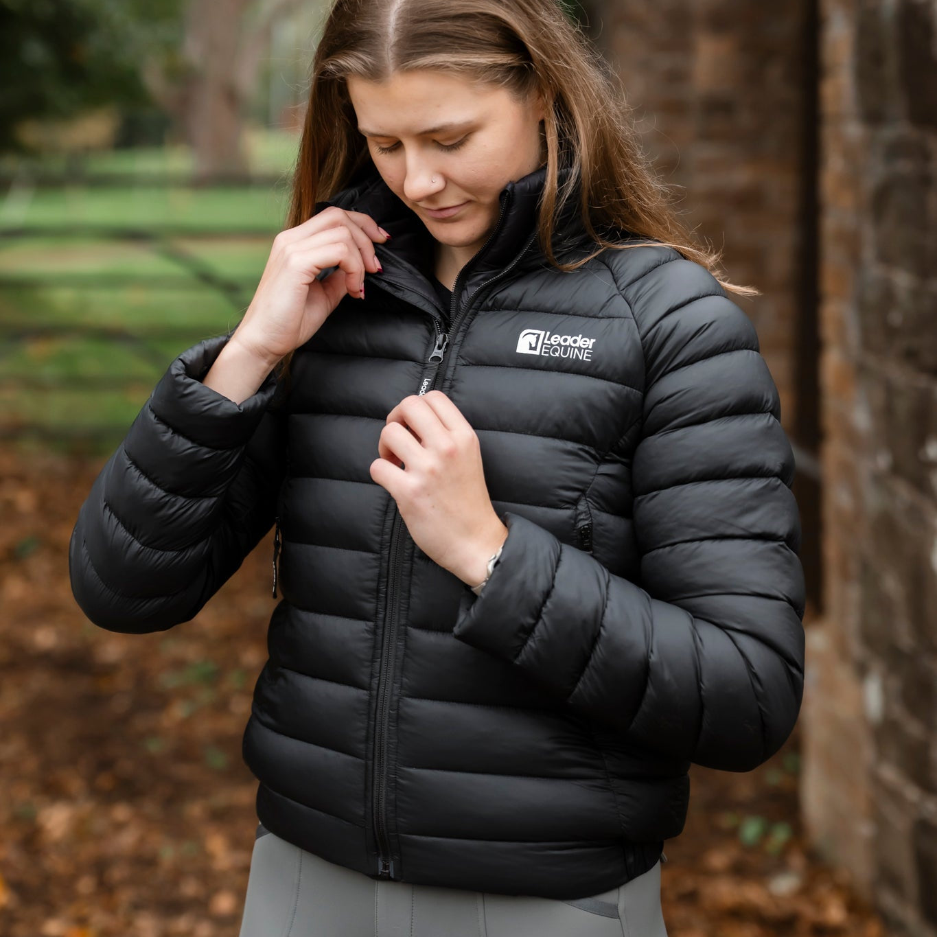 Woman wearing a black puffer jacket with a brand logo in an outdoor setting.