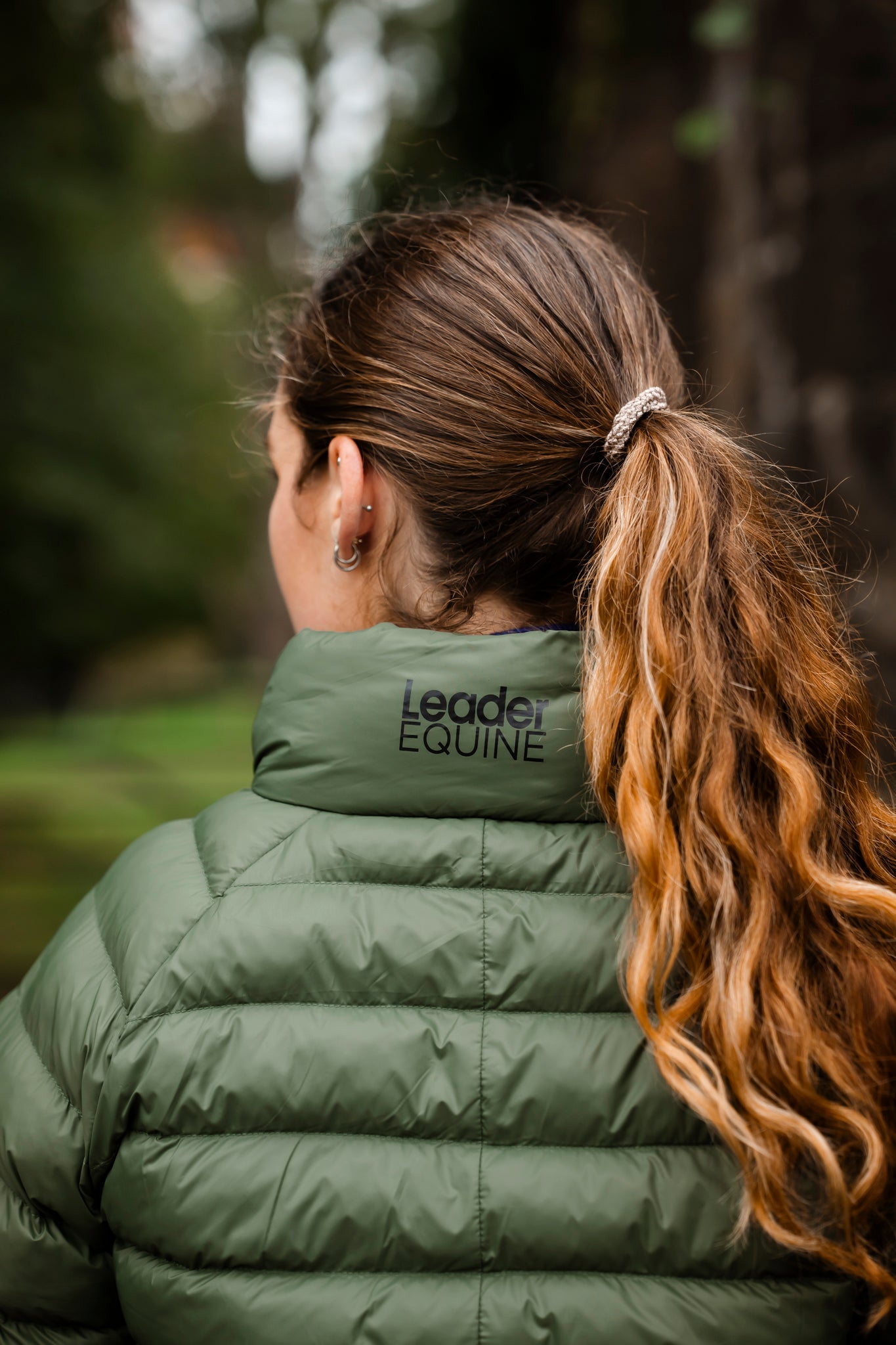 Person wearing a green puffer jacket with 'Leader Equine' branding, standing outdoors.