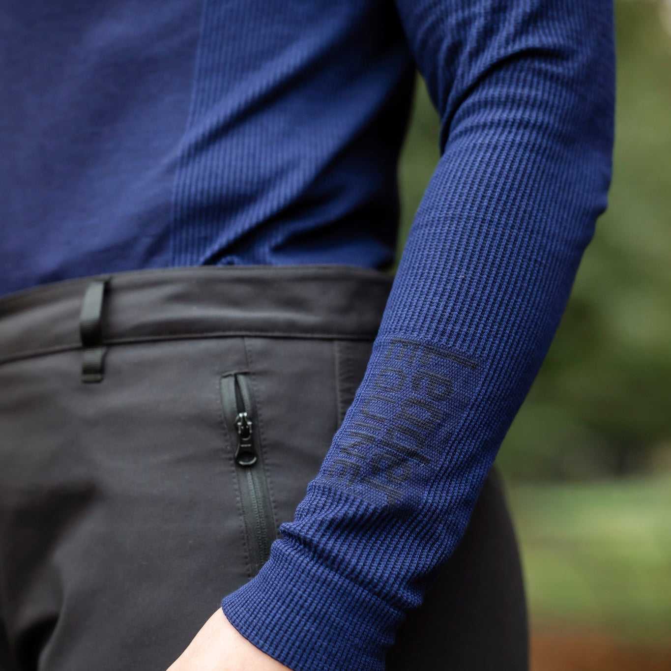 Person wearing a blue long-sleeve shirt and dark pants with a blurred natural background