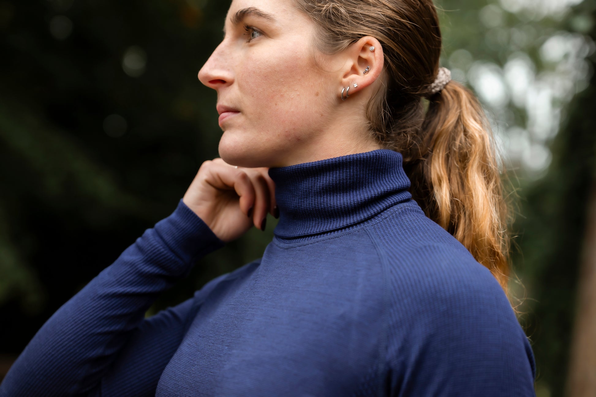 Woman wearing a blue leader equine sweater outdoors with blurred greenery in the background