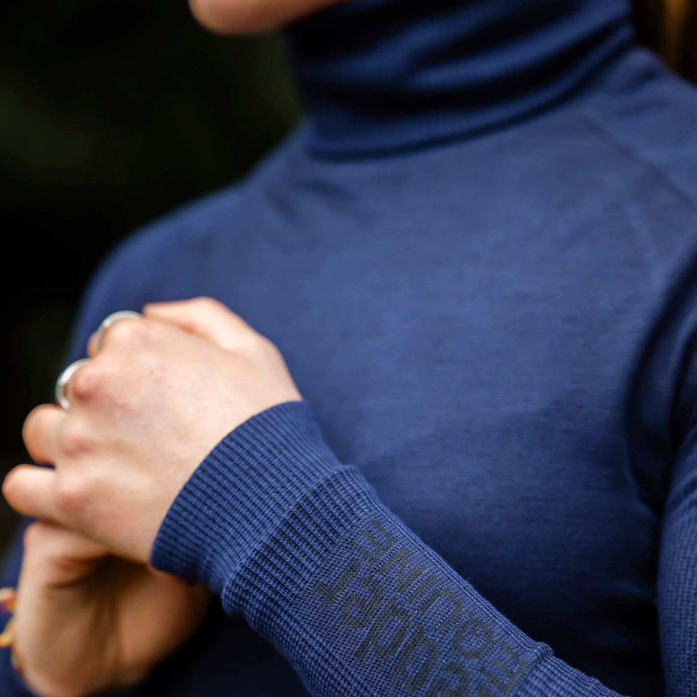 Close-up of a person wearing a blue leader equine baselayer with high neck with a brand logo on the sleeve.