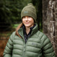 Person wearing a green puffer jacket and beanie standing in a forest.