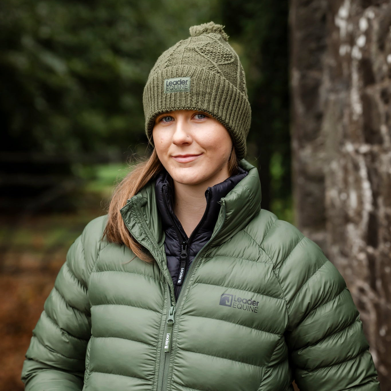 Person wearing a green puffer jacket and beanie standing in a forest.