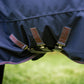 Close-up of a blue leader equine boxter turnout horse blanket with extra belly protection, triple straps and visible branding on a blurred green background.