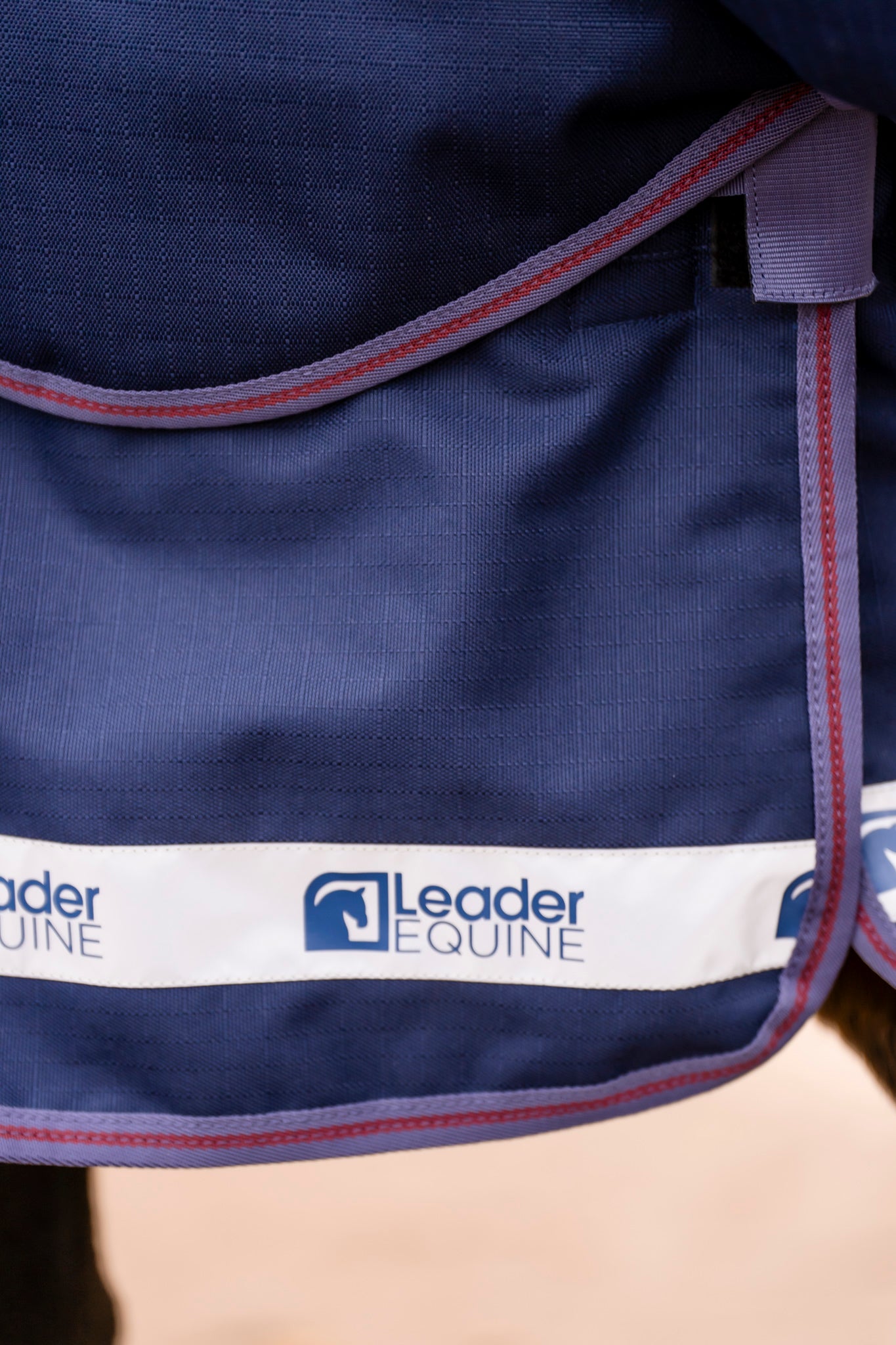 Navy blue equestrian blanket with Leader Equine logo on a white band.
