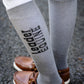 Gray knee-high socks with 'Leader Equine' text worn by a person on a dark surface.