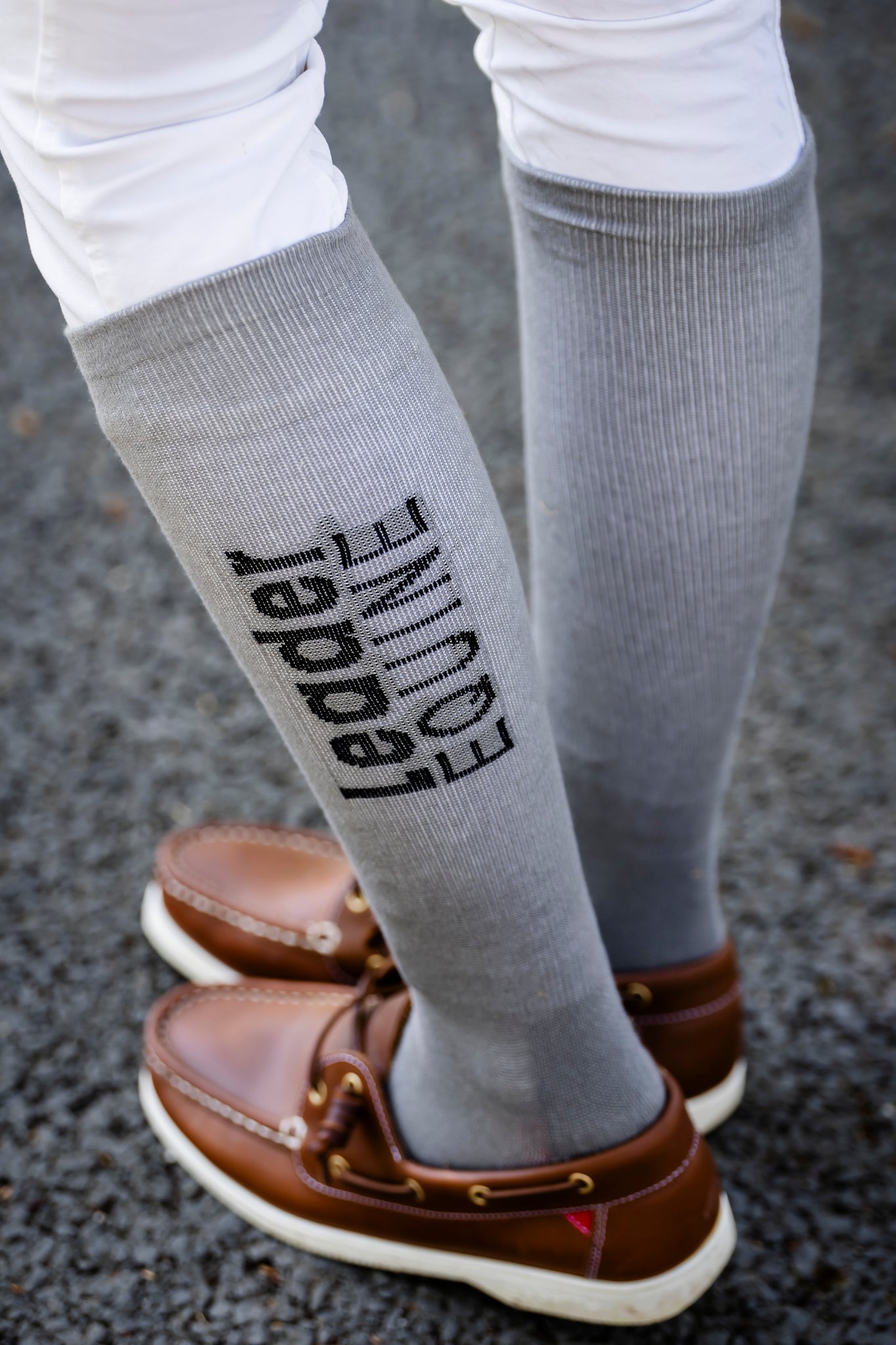 Gray knee-high socks with 'Leader Equine' text worn by a person on a dark surface.