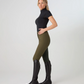 A woman modeling high-waisted ps of sweden olive green riding breeches with a black short-sleeve mock neck top and black riding boots, shown in profile against a light gray studio background.