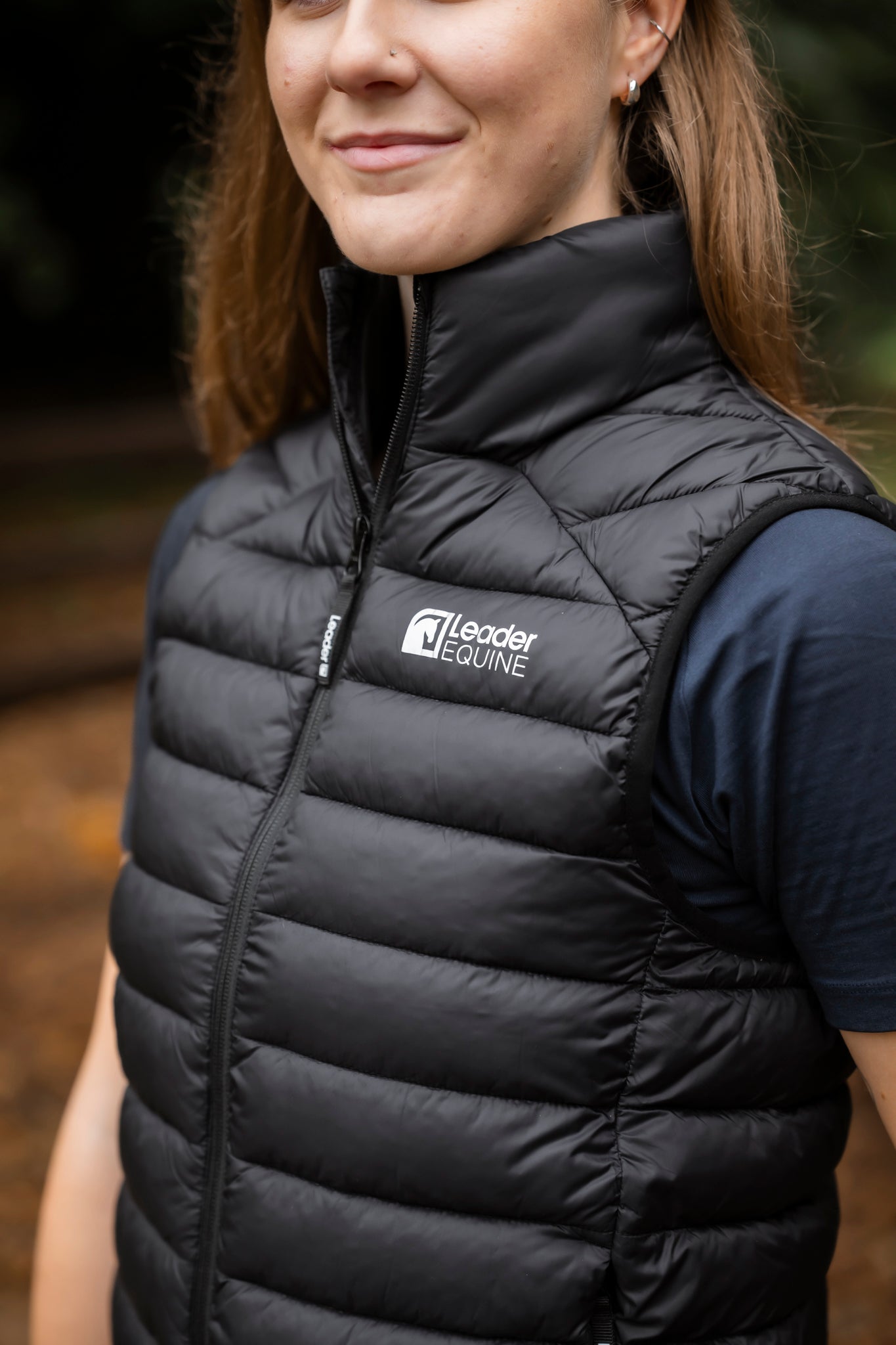 Person wearing a black puffer vest with Leader Equine logo outdoors