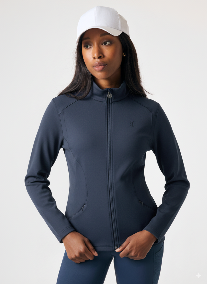 Woman wearing a dark blue athletic jacket and pants with a white cap on a light gray background