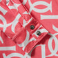 Close-up of a pink top with white geometric pattern and buttons.