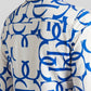 A close-up of a white long-sleeve button-up shirt with a bold blue abstract interlocking pattern, shown on a model from the back.