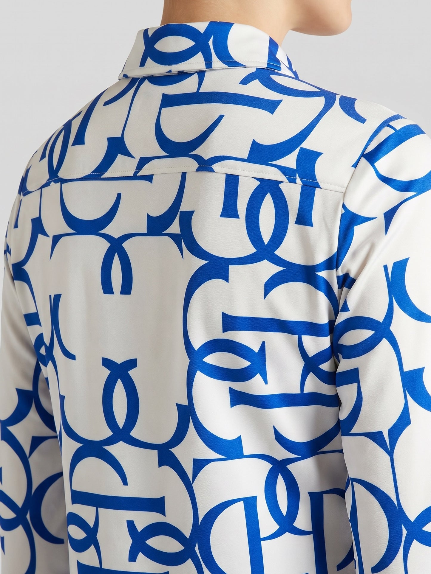 A close-up of a white long-sleeve button-up shirt with a bold blue abstract interlocking pattern, shown on a model from the back.