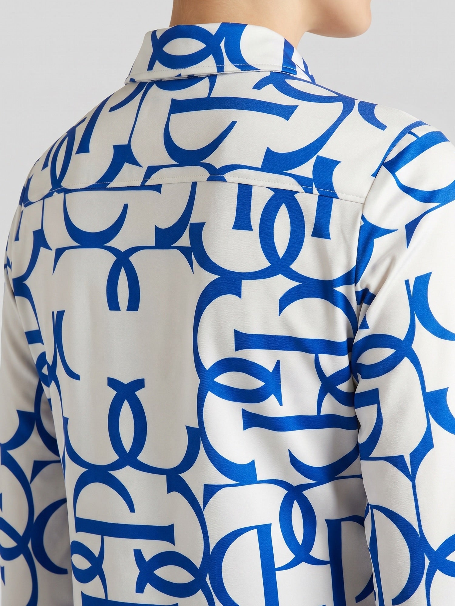 A close-up of a white long-sleeve button-up shirt with a bold blue abstract interlocking pattern, shown on a model from the back.