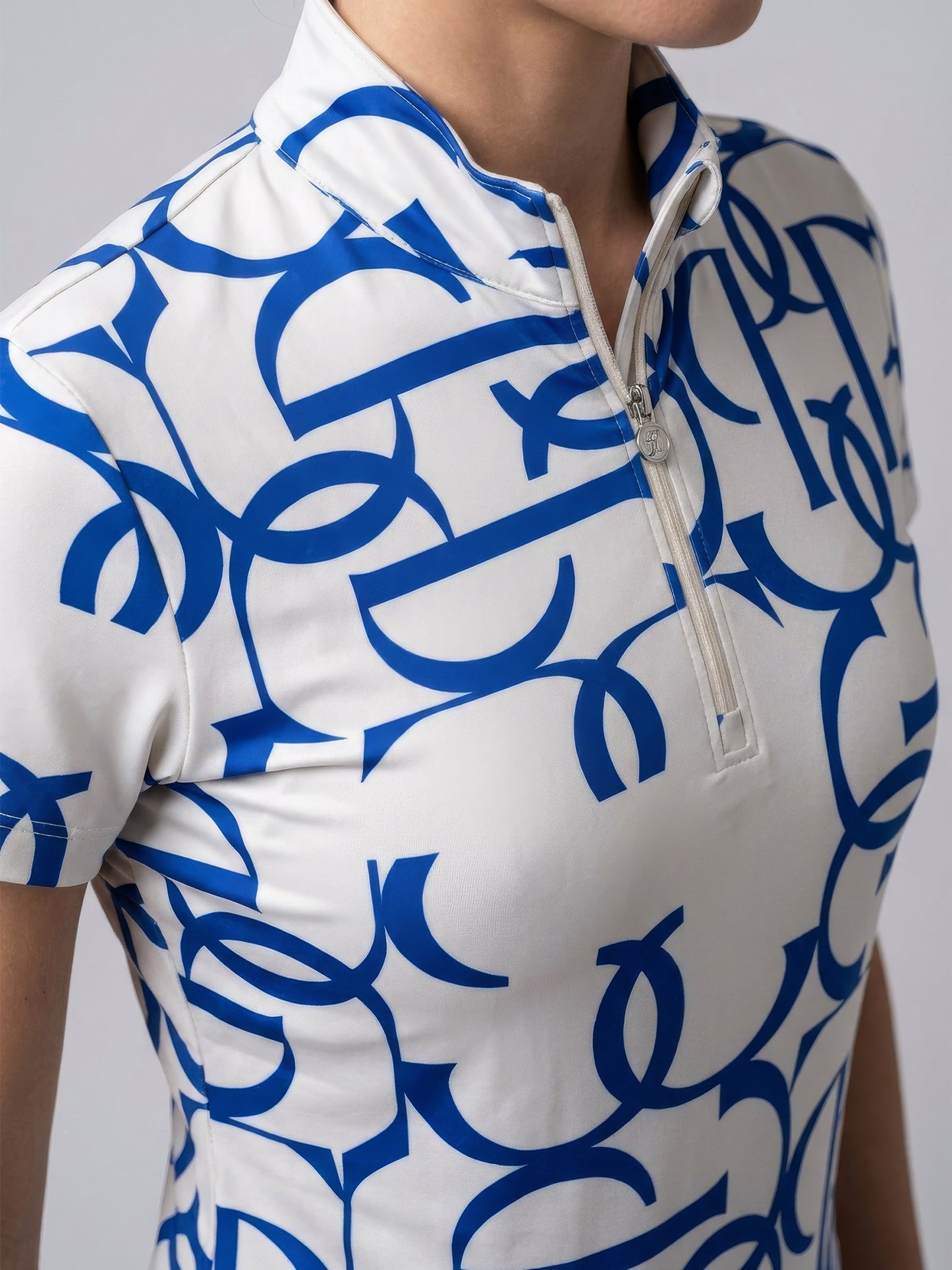 A close-up of a model wearing a short-sleeve athletic top with a white base and a bold blue abstract pattern, featuring a white half-zip collar.